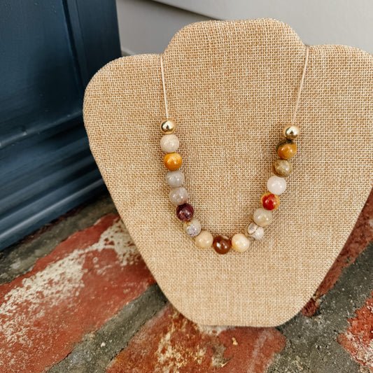 Necklace with multicolored beads on a beige display stand against a neutral background